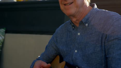 active senior man playing guitar in the balcony at home 4k