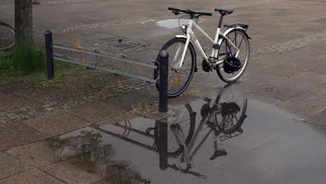 bicycle next to a bike stand with its reflection in a puddle of rain, wide shot