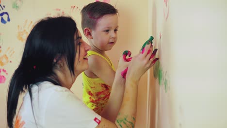 madre feliz y su lindo niño divirtiéndose juntos dejando sus coloridas huellas de manos y pintando en la pared. joven familia feliz. concepto de madre e hijo