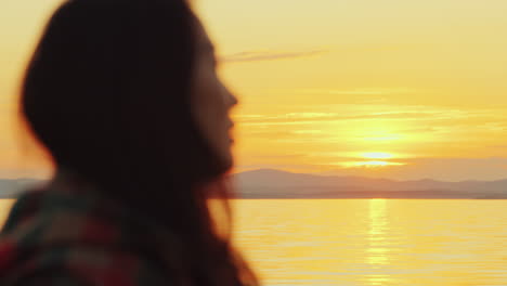 vista de perfil de una joven asiática contemplando la puesta de sol sobre el lago y las montañas