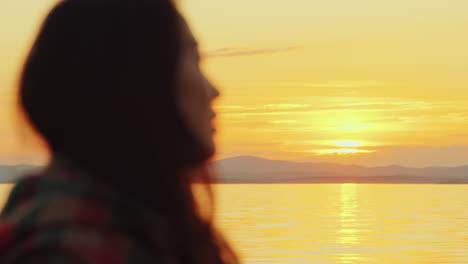 profile view of young asian woman contemplating sunset over lake and mountains