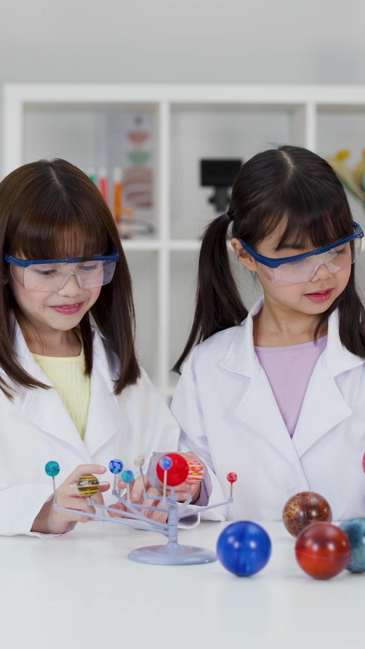 Dua siswa mengenakan kacamata pengaman memeriksa model planet selama proyek kelas sains.