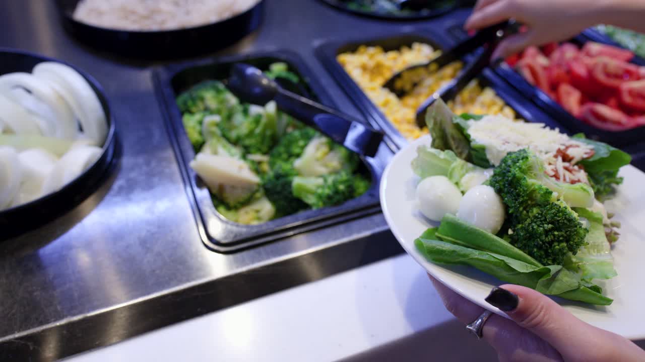 Primo piano di una donna che aggiunge verdure fresche miste al buffet dell'insalata con illuminazione dall'alto