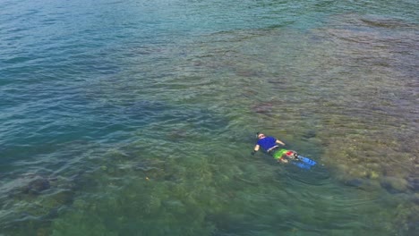 Aerial-view-above-man-snorkelling-in-turquoise-Panama-island-coral-reef-ocean-waters