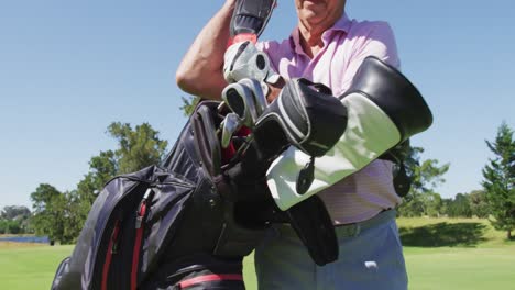 hombre mayor caucásico caminando con su bolsa de golf en el campo de golf en un brillante día soleado