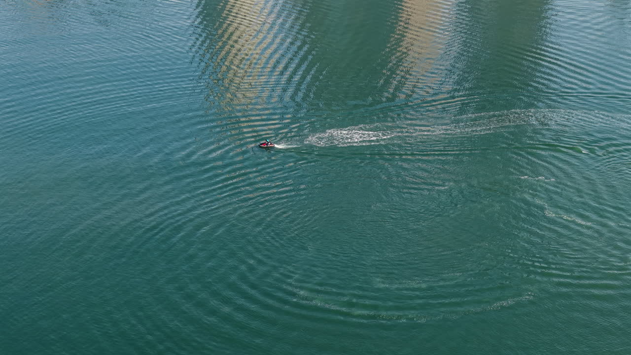 A high-angle aerial drone shot of a person riding a jet ski at speed across the beautiful turquoise water of the bay in Itapema, Santa Catarina, Brazil