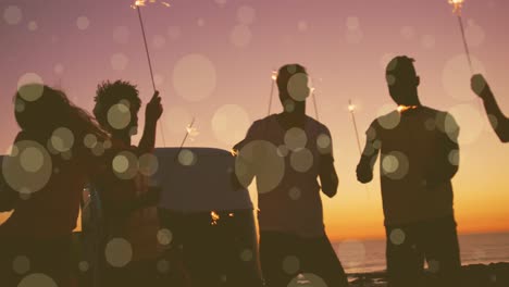 Animation-of-yellow-spots-of-light-over-friends-dancing-with-new-year-sparklers-on-beach