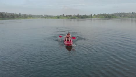 aerial shot tracking a white man from in front adventuring on a red kayak paddling on the river nile