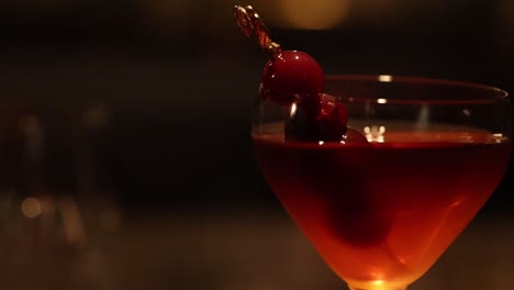 a close-up of a cocktail with cherry garnish, set against a softly lit background.