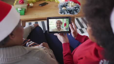 madre y hija afroamericanas usando una tableta para una videollamada de navidad con un hombre en la pantalla