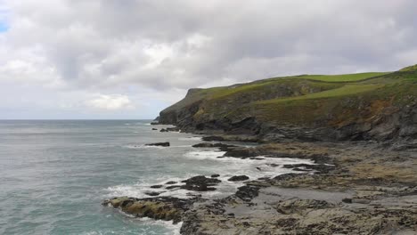 An-aerial-shot-of-the-crashing-waves-at-Pentire-Point-near-Polzeath-beach,-displaying-an-amazing-coastline