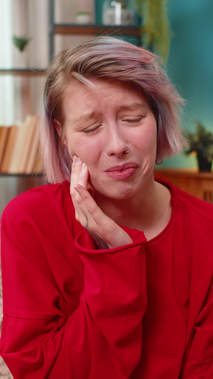Young woman holding cheek experiencing toothache pain painful uncomfortable facial expression home
