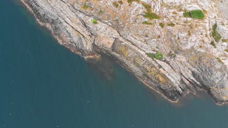 Toma-Aérea-De-Rocas-Escarpadas-Que-Salen-Del-Agua-Azul-Clara-Con-Escasa-Vegetación