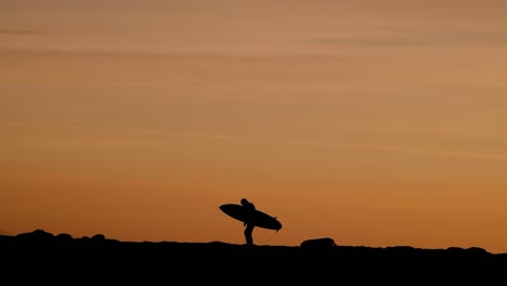 silueta de surfista al atardecer caminando sobre rocas