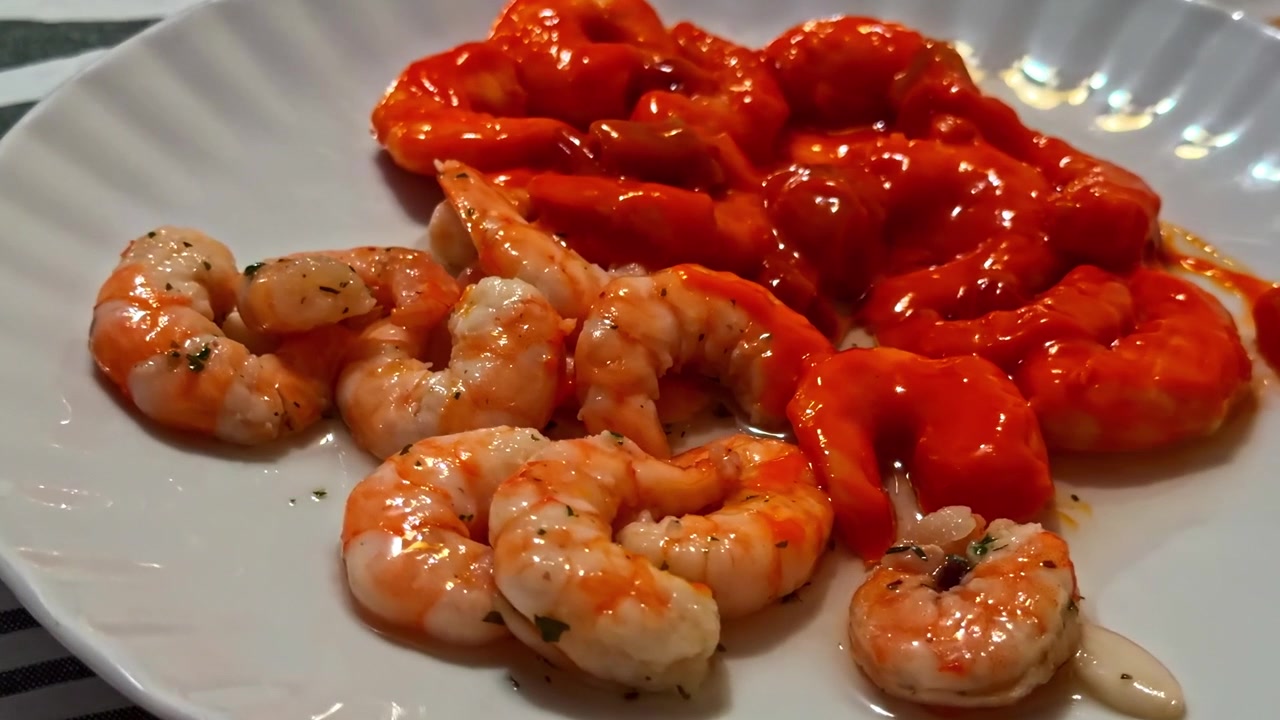 Gamberi cotti serviti con una ricca salsa di pomodoro su un piatto bianco su una tovaglia a righe.