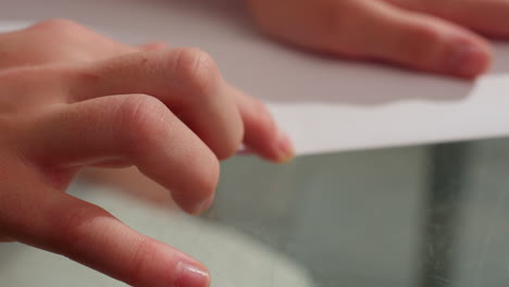 Close-up view of hand carefully straightening fold on paper, focused on precision during paper crafting project on glass table
