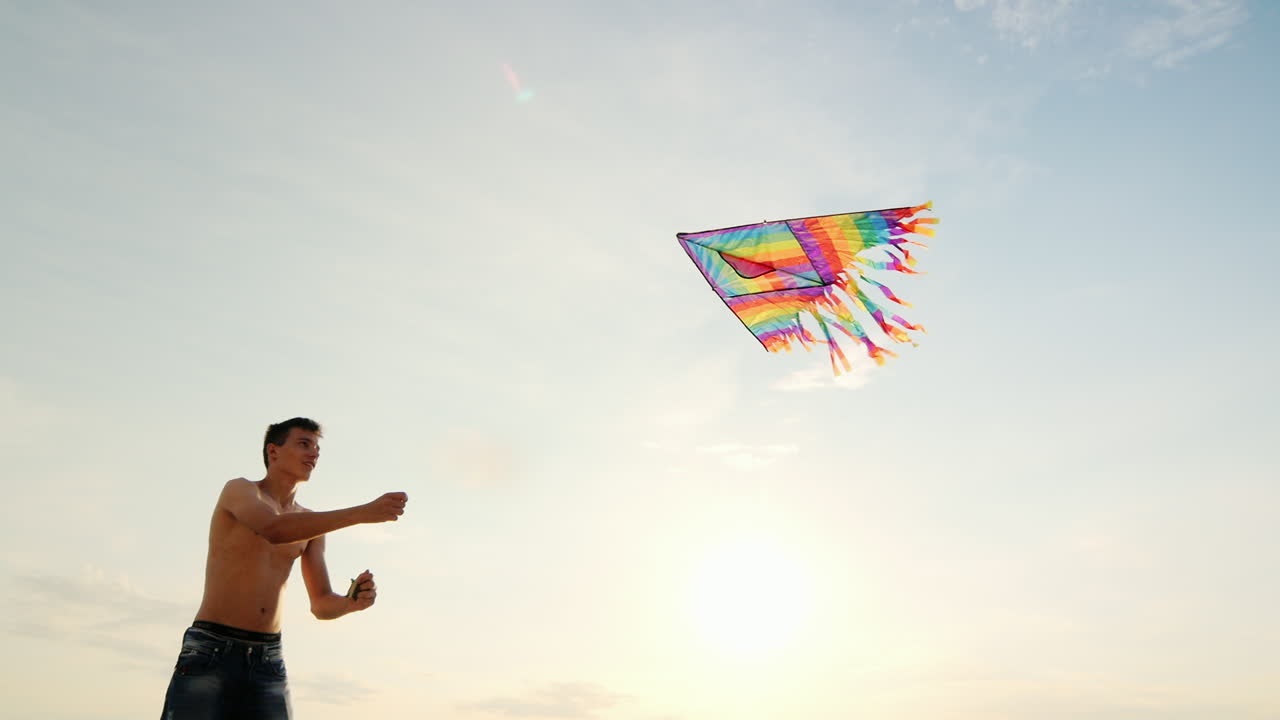 niño adolescente jugando con una cometa contra el fondo del cielo azul vista desde abajo