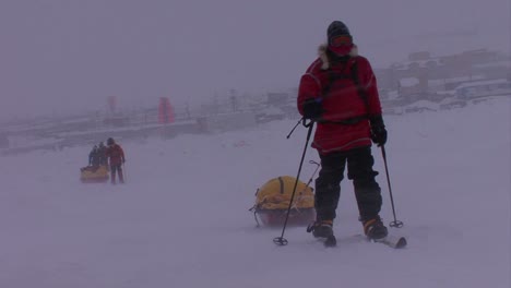 an arctic expedition moves across frozen tundra on cross country skis towing supplies near a town