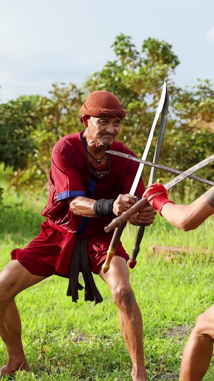 Un guerriero in costume rosso esegue una danza rituale con due spade all'aperto.