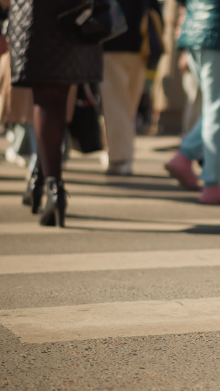 Gambe di passanti e borse che attraversano le strisce pedonali, tacchi alti e stivali che battono sul marciapiede, borsa trapuntata con tracolla a catena, cappotto sartoriale e collant lavorati, luce pomeridiana e traffico pedonale intenso