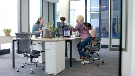 high-fiving and celebrating success, diverse colleagues in modern office workspace