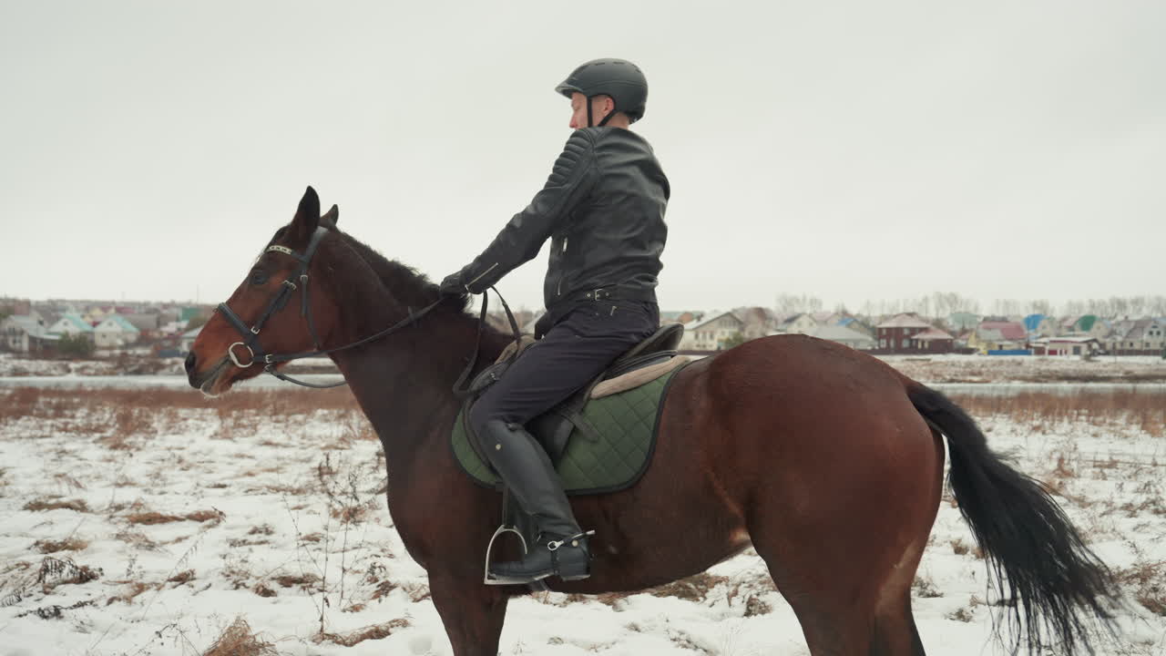 Всадник обнимает лошадь перед посадкой. Всадник в шлеме устанавливает нежную связь с гнедой лошадью на заснеженной равнине, затем садится верхом и едет с уверенной осанкой во время совместного учебного занятия, тренер рядом.