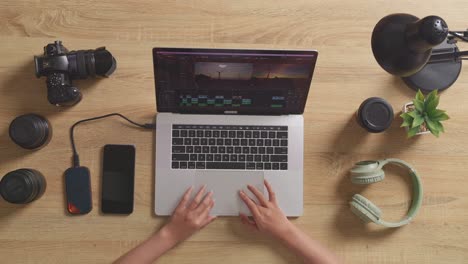 top view close up of woman editor's hands using a laptop next to the camera editing the video in the workspace at home