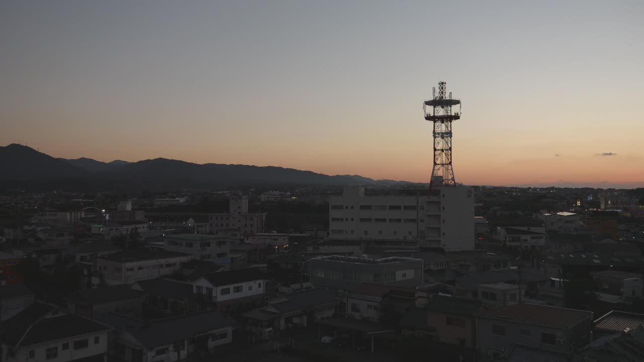 el anochecer se asienta sobre una ciudad con una prominente torre de comunicación siluetada contra un cielo que se desvanece en izumi, kyushu, japón