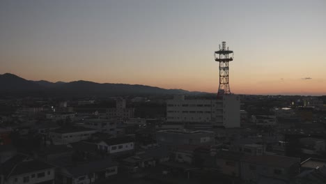 Die-Dämmerung-Senkt-Sich-über-Eine-Stadt-Mit-Einem-Markanten-Kommunikationsturm,-Der-Sich-Vor-Einem-Verblassenden-Himmel-In-Izumi,-Kyushu,-Japan,-Abhebt