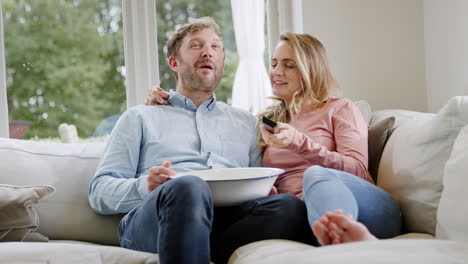 en una noche de pareja sentados en el sofá en casa riendo y viendo una película en la televisión con palomitas de maíz