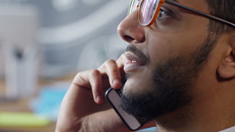 Vista-De-Cerca-Del-Hombre-árabe-Con-Gafas-Sentado-En-El-Estudio-Hablando-Por-Teléfono