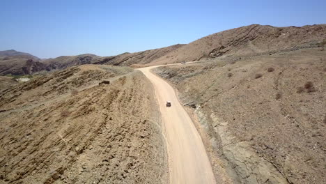 4k footage of a jeep driving along a dusty road in namibia, captured from a drone following the vehicle. the breathtaking rocky landscape and expansive views the rugged beauty of this african terrain.