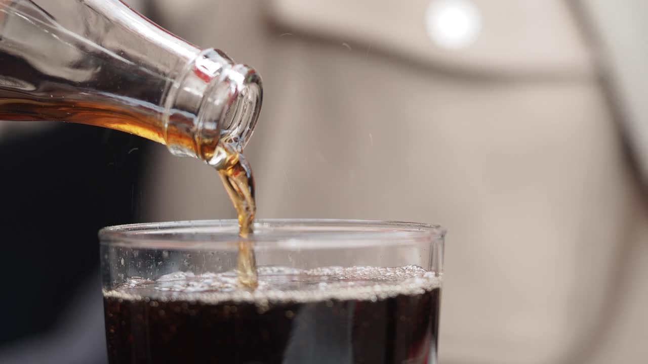 Versare cola frizzante da una bottiglia di vetro in un bicchiere trasparente