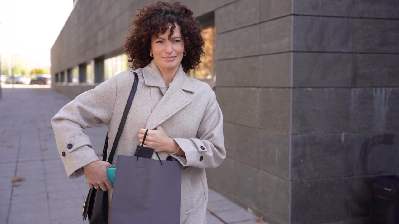 Una donna alla moda cammina felicemente all'aperto in città con una shopping bag elegante.