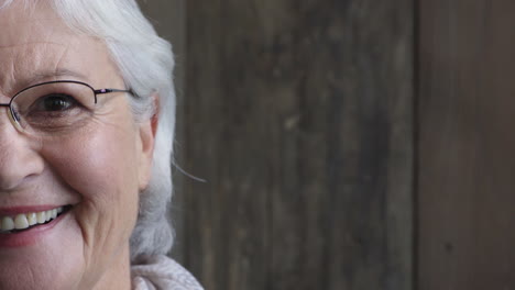 half face portrait of happy elderly woman laughing looking at camera cheerful wearing glasses on wooden background