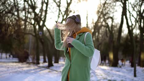 mujer alegre baila en winter park, escuchando música por teléfono usando auriculares