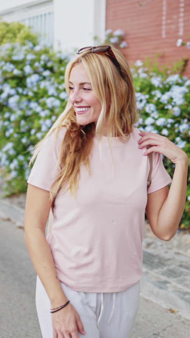 Giovane donna bionda felice che cammina e sorride su una strada soleggiata.