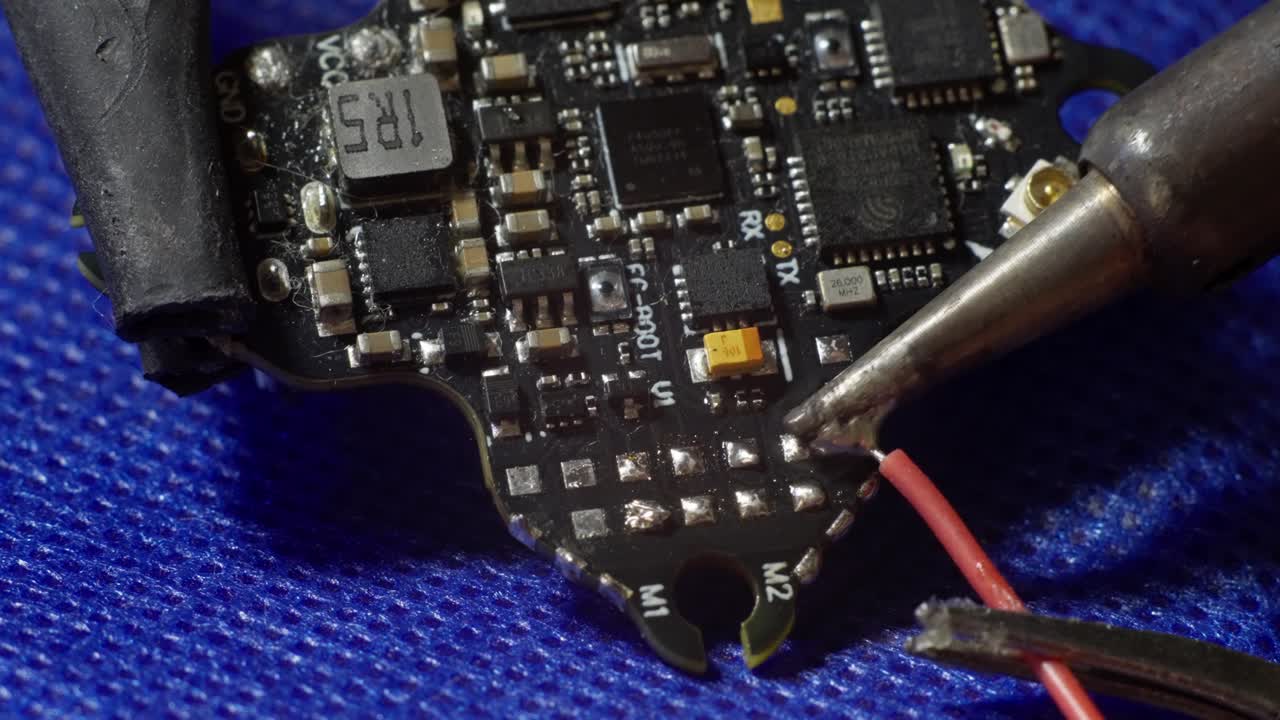 CLOSE UP SHOT OF A MAN SOLDERING A RED CABLE INTO A FLIGHT CONTROLLER OF AN FPV DRONE