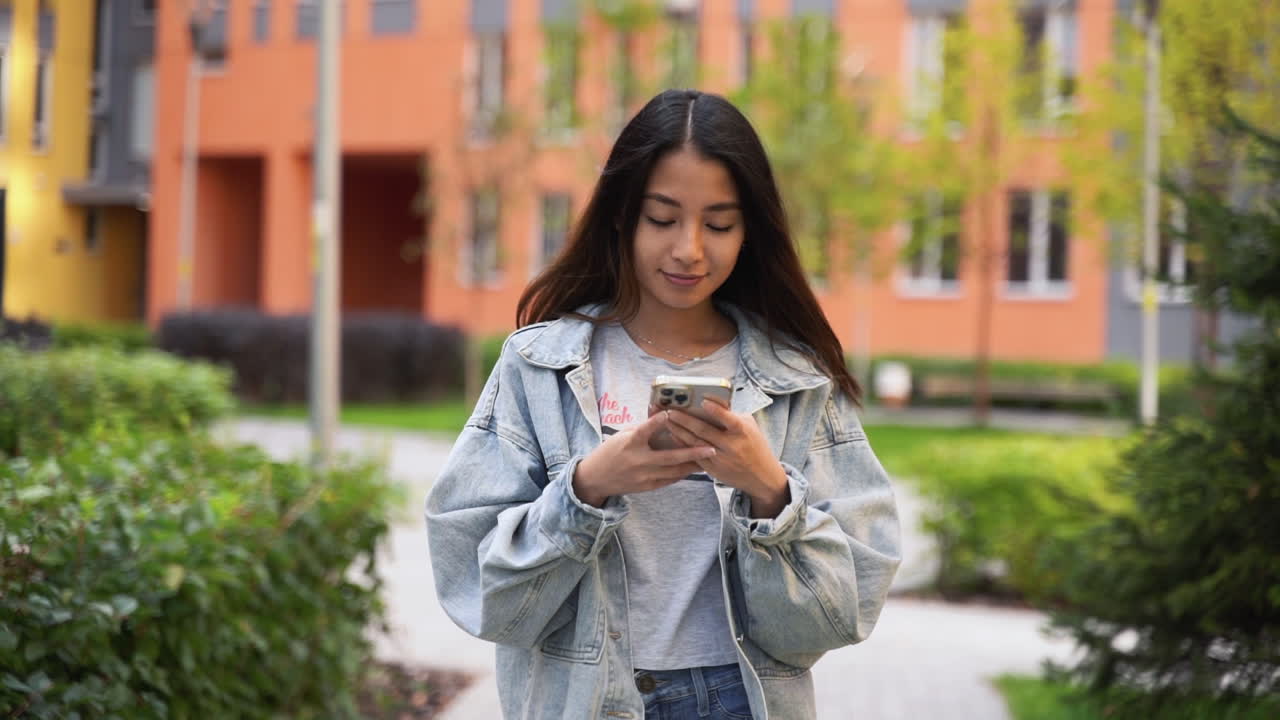 hermosa joven japonesa enviando mensajes de texto en el teléfono móvil mientras camina al aire libre