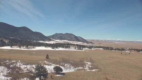 Drone-view-of-a-snowy-brown-meadow-in-Colorado-with-mountains-in-the-background