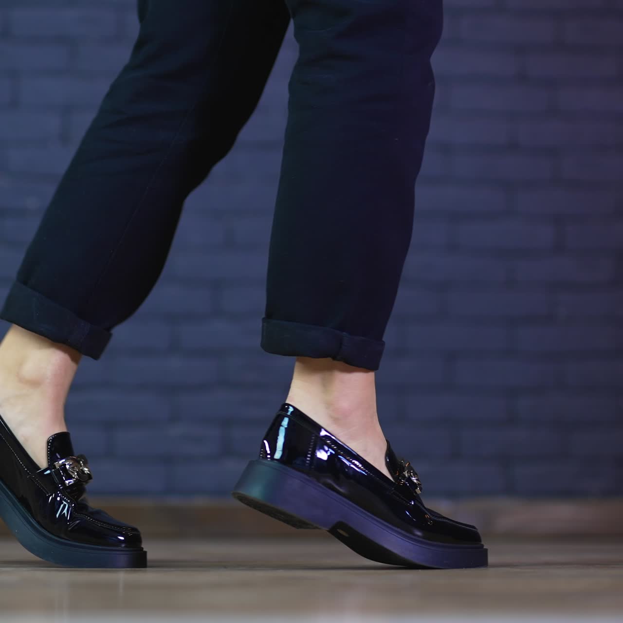 Female model's legs wearing blue fashionable jeans and low-heeled shoes. Black shining shoes decorated with massive silver chain demonstration