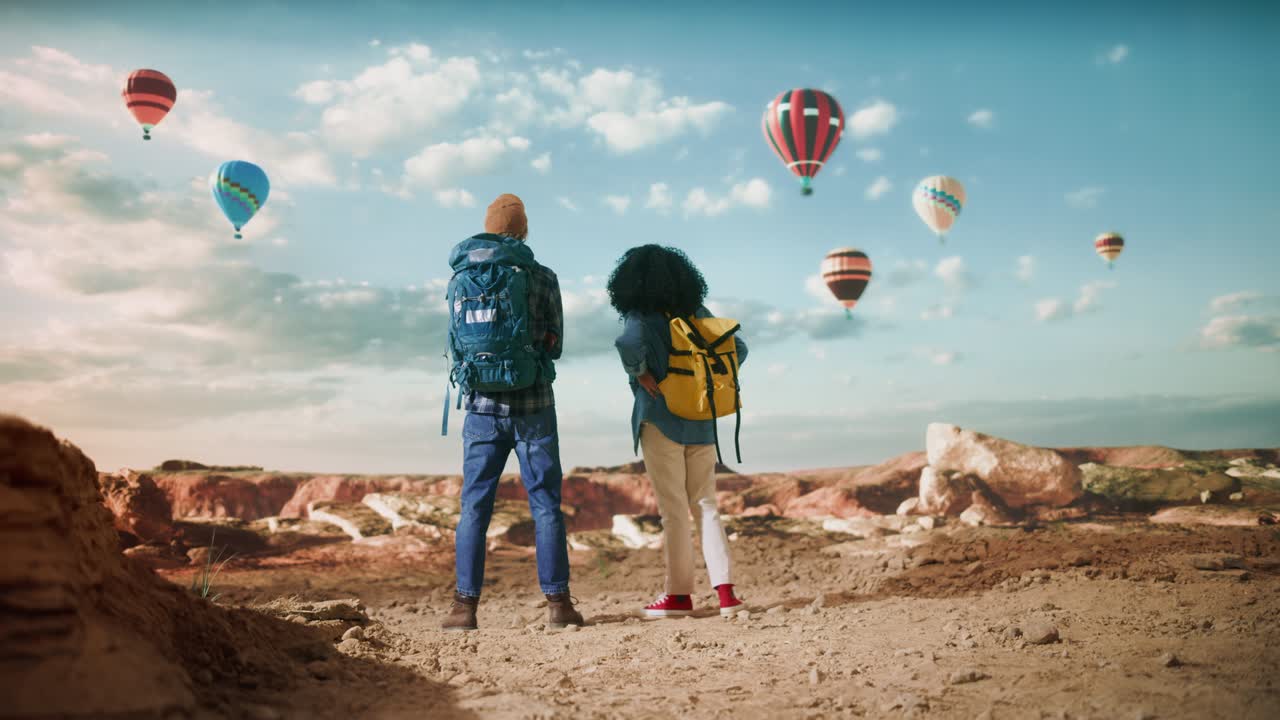 una joven pareja de turistas diversos caminando con mochilas en el gran desierto en el valle rocoso del cañón. amigos mochileros masculinos y femeninos en un viaje de aventura. festival de globos de aire caliente en el parque nacional de la montaña.