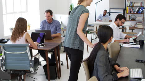 Woman-walks-past-and-greets-colleagues-working-in-office