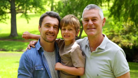 Three-generations-of-men-smiling-at-camera-in-the-park