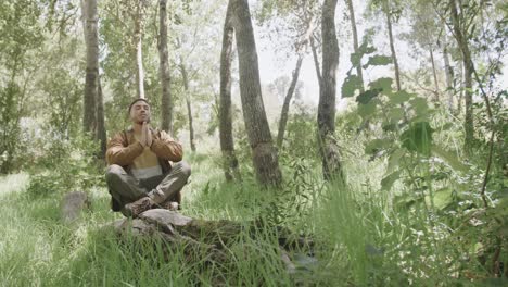 hombre afroamericano sentado en el tronco de un árbol y meditando en el bosque, cámara lenta