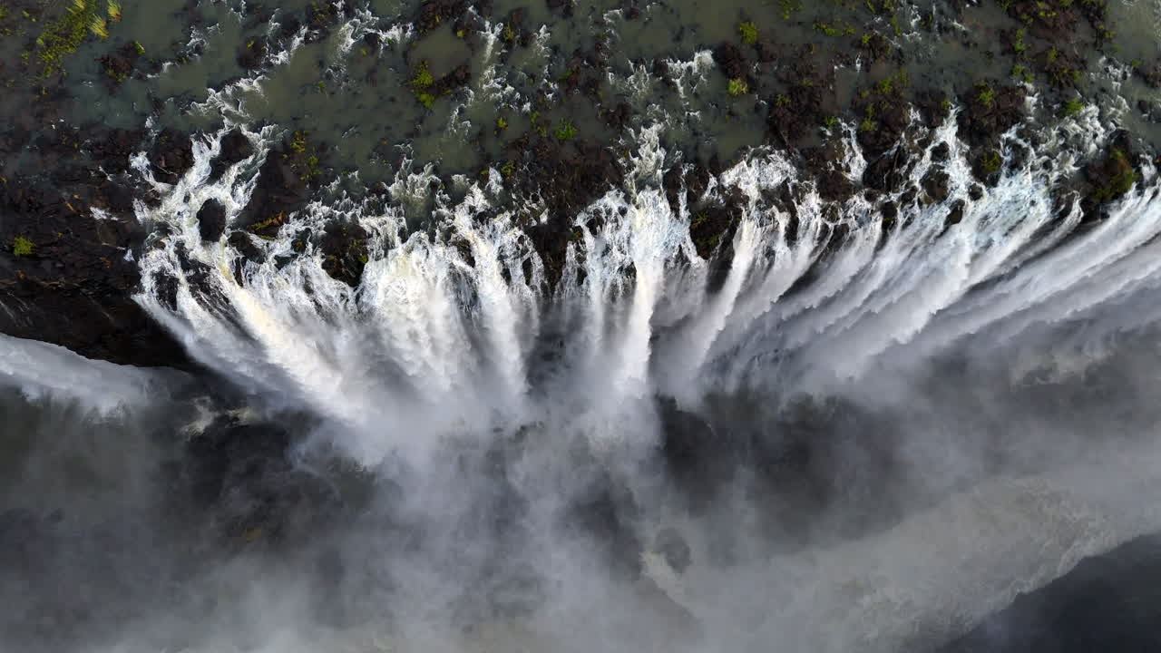 Aerial view of Victoria Falls with powerful waterfall plunging into gorge, mist rising above lush green forest, dramatic natural wonder and iconic travel destination in Africa