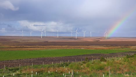 a beautiful rainbow forms near wind generation windmills in northern scotland