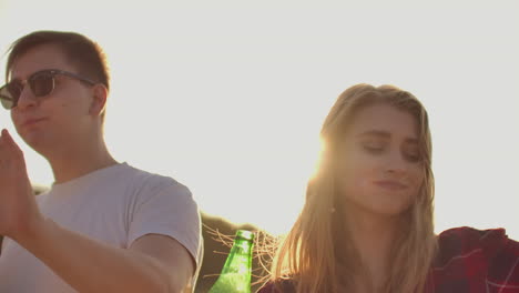 A-young-man-is-dancing-in-trendy-black-sun-glasses-and-white-T-shirt-with-beer-on-the-open-air-party-with-a-beautiful-young-blonde-girls-with-long-hair.-They-spend-time-cheerfully-and-carefree.