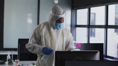 health worker wearing protective clothes and face mask cleaning computer with cloth and disinfectant