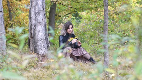 brunette girl in the autumn forest holds a yellow leaf in her hand and hides her face behind it - wide shot